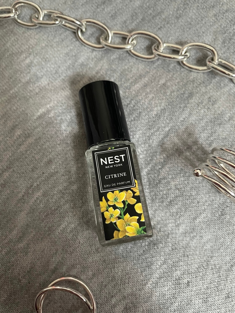 A picture of the travel size fragrance Citrine from NEST New York Fragrances on a gray background surrounded by silver jewelry. 